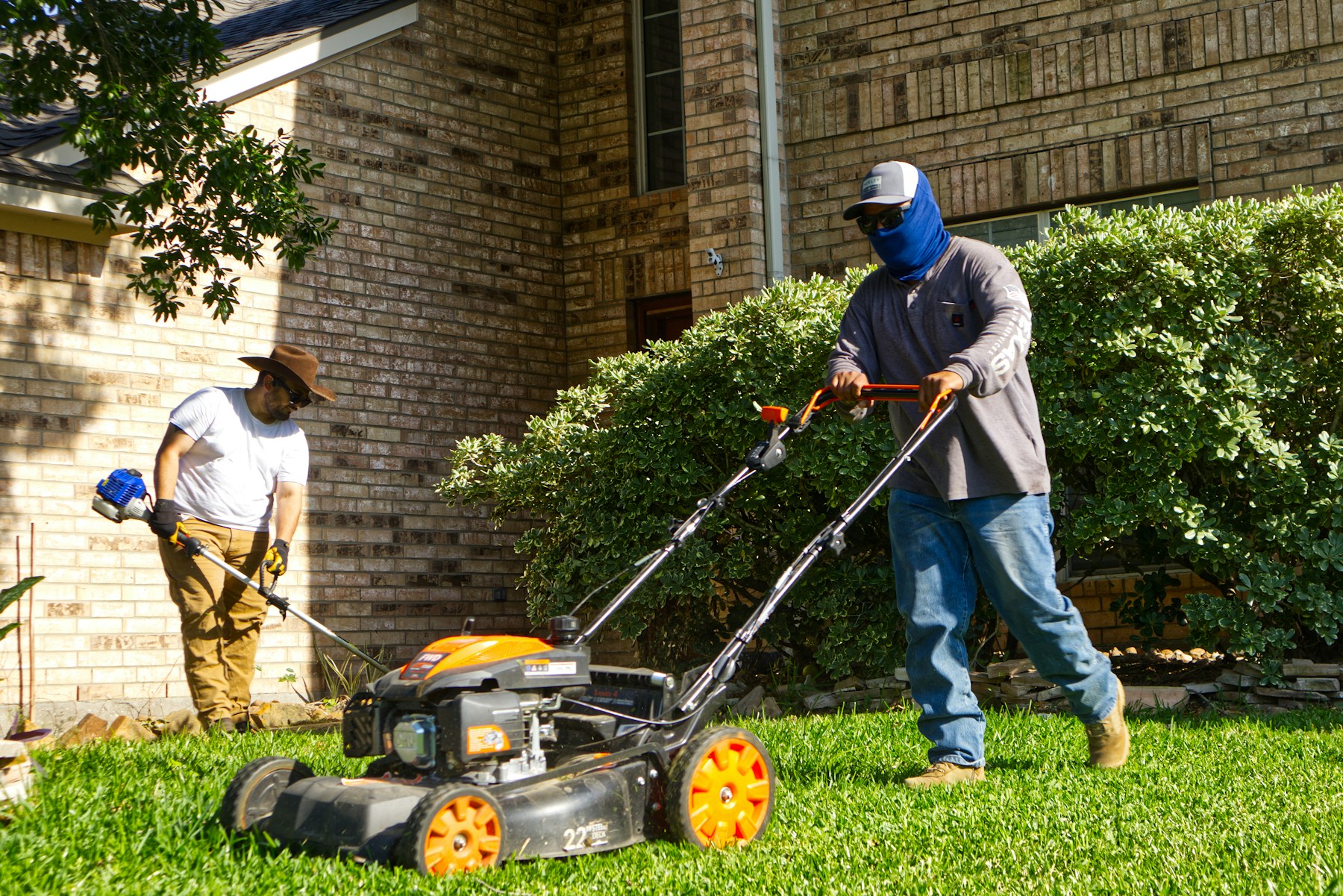 Two professional lawn care workers operating a commercial mower on a residential property